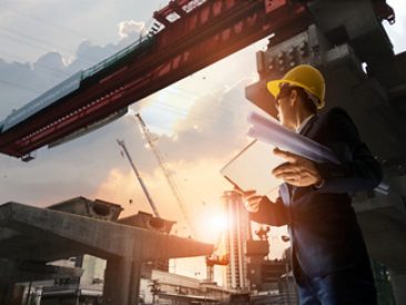 Construction engineer manager supervising progress of BTS Station Construction Project and tablet with blueprint in hands. Cranes in sunset background. Industrial technology 4.0