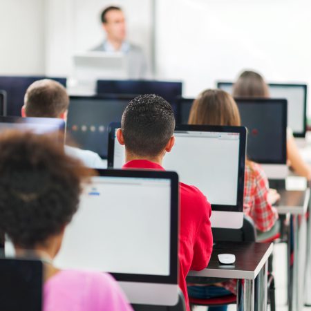 Rear view of lager group of people at a computer class. Teacher is teaching in the background.